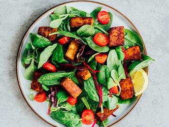 plate of colourful salad including tofu, tomatoes and salad leaves